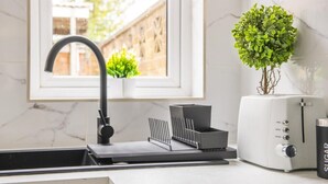 Uma cozinha moderna com pia embutida, janela com vista para o verde, torradeira e um vaso de planta.