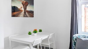 Uma mesa de jantar branca com três vasos de plantas, uma cadeira branca e um quadro de um elefante na parede.