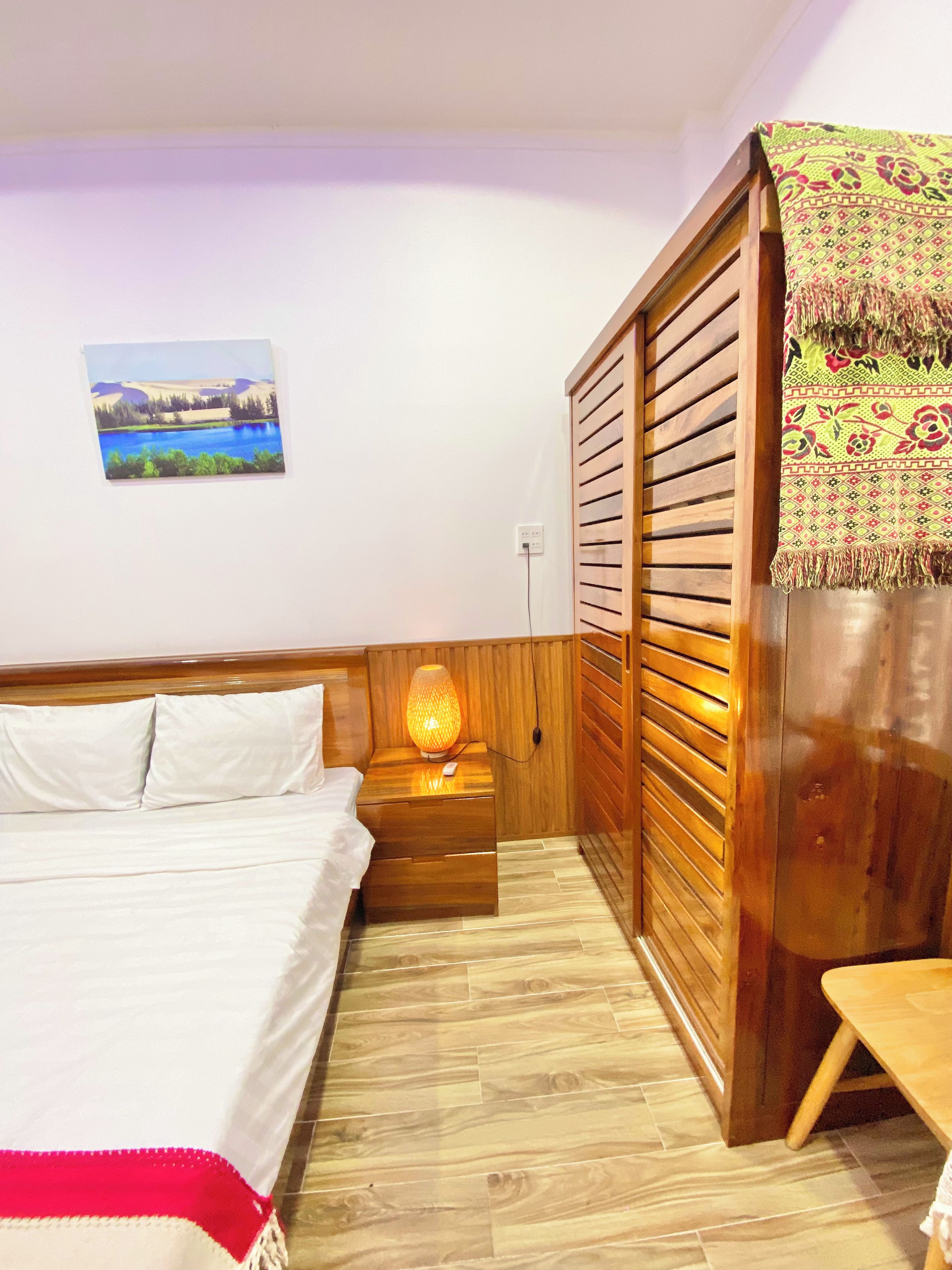 A bedroom with a bed, bedside table, lamp, and a view of a landscape painting.