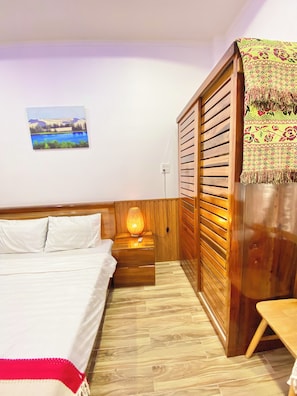 A bedroom with a bed, bedside table, lamp, and a view of a landscape painting.