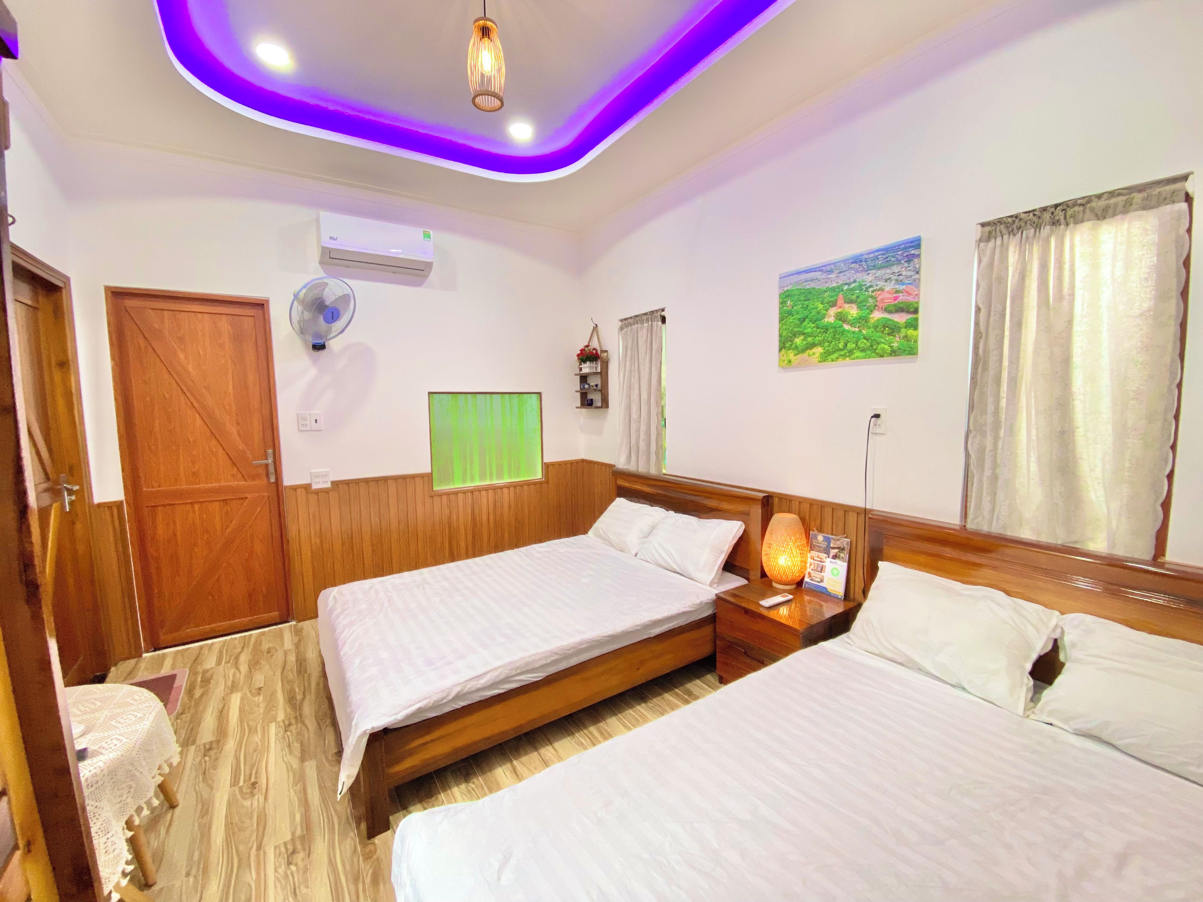 A hotel room with two beds, wooden paneling, a ceiling fan, an air conditioning unit, and a painting on the wall.