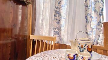 A table with a lace tablecloth, two ceramic mugs with rooster designs, and a ceramic teapot with a floral pattern.