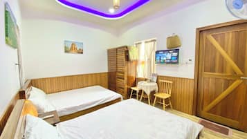 A room with two beds, a wooden wardrobe, a television on the wall, and a ceiling with purple lighting.