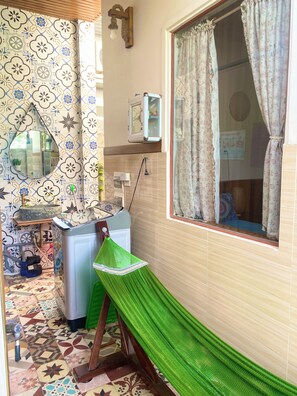 A bathroom with a patterned tile floor, a green hammock, a washing machine, and a window with floral curtains. - Sea-breeze homestay (Phu Thuy)