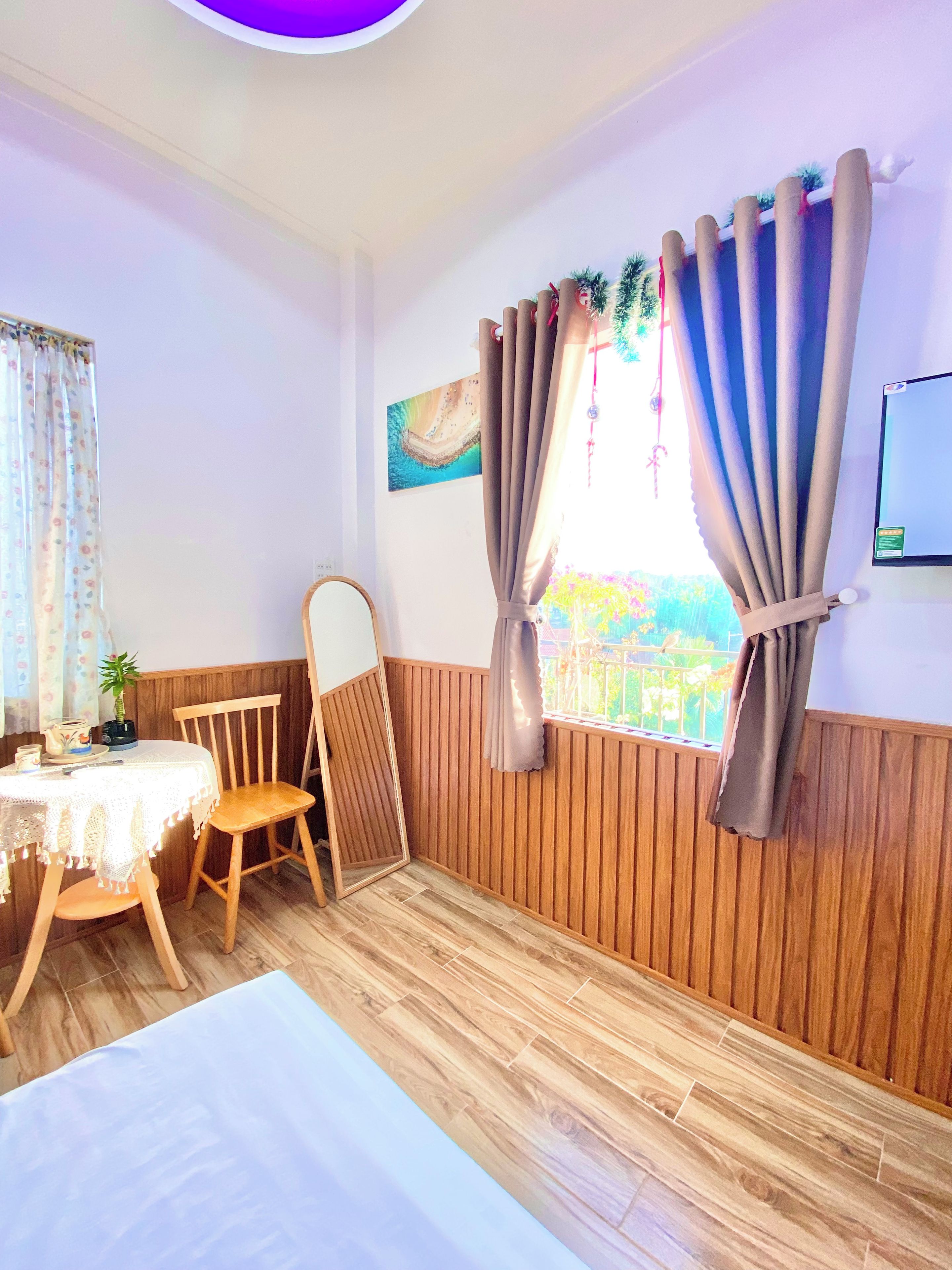 A room with a bed, a wooden chair, a small table with a plant, and a window with curtains.
