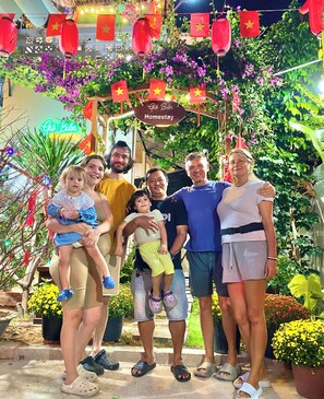 A group of people standing in front of a sign with Vietnamese text, surrounded by greenery and red lanterns. - Sea-breeze homestay (Phu Thuy)