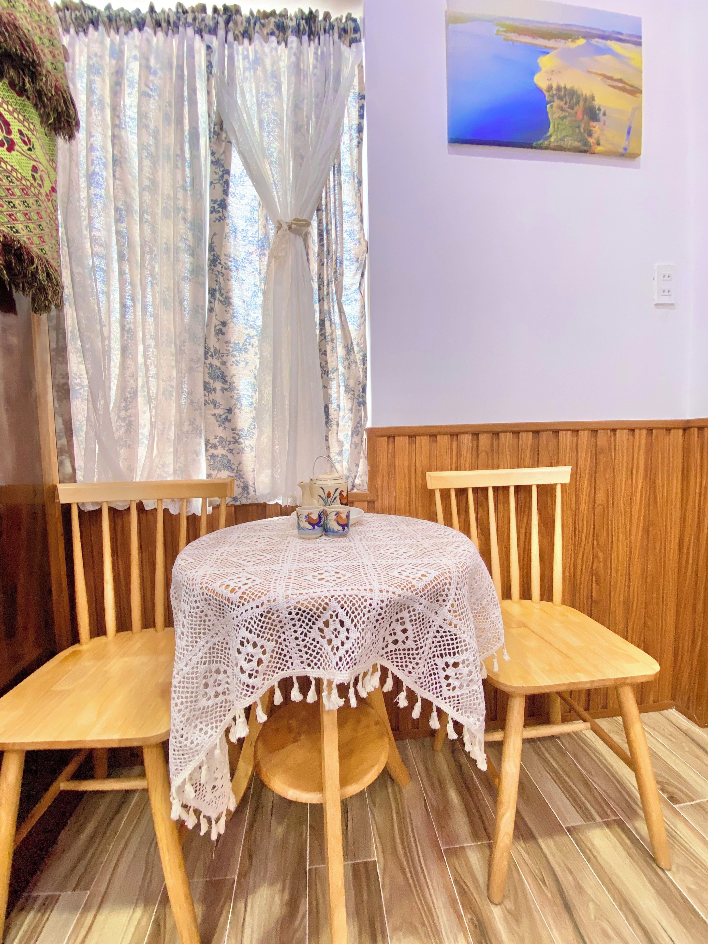 Une table ronde en bois recouverte d’une nappe en dentelle blanche, deux chaises en bois et un vase contenant des objets décoratifs posé sur la table.