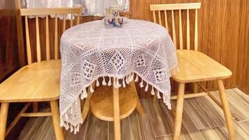 Une table ronde en bois recouverte d’une nappe en dentelle blanche, deux chaises en bois et un vase contenant des objets décoratifs posé sur la table.