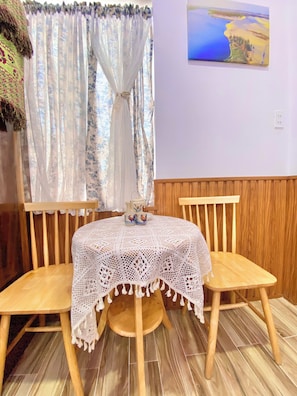 A round wooden table with a white lace tablecloth, two wooden chairs, and a vase with decorative items on the table. - Sea-breeze homestay (Phu Thuy)