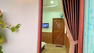 A room with a wooden floor, a bed, a television, and a door with a curtain.