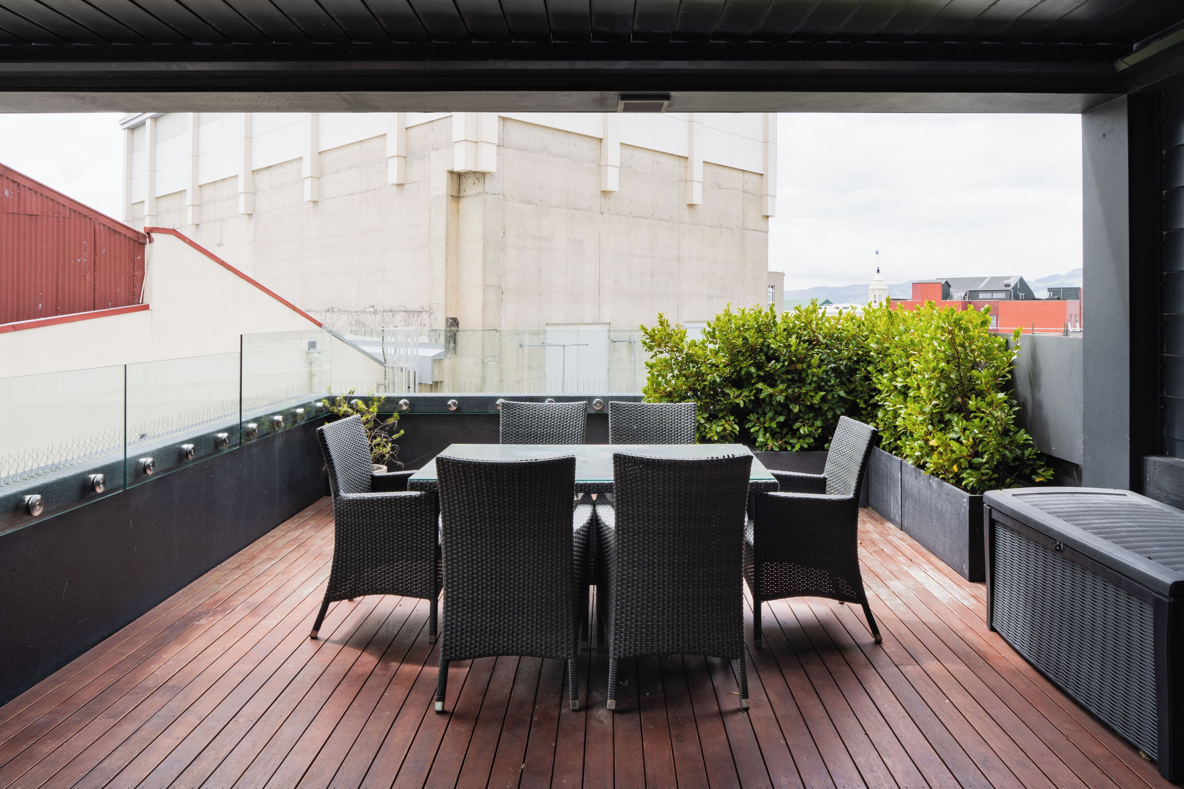 An outdoor patio with a table and chairs, surrounded by greenery and overlooking a cityscape.