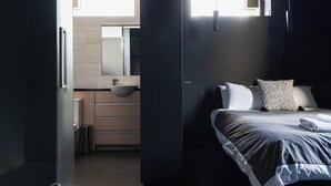 A modern bedroom with a large bed, a bedside table, a built-in sink, and a window providing natural light. - Deluxe Inner-city Apartment on Moray (Dunedin)