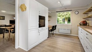 Eine kleine Küche mit weißen Schränken, einem eingebauten Backofen, einem Essbereich mit Tisch und Stühlen sowie einem Fenster mit Blick auf Grünflächen.