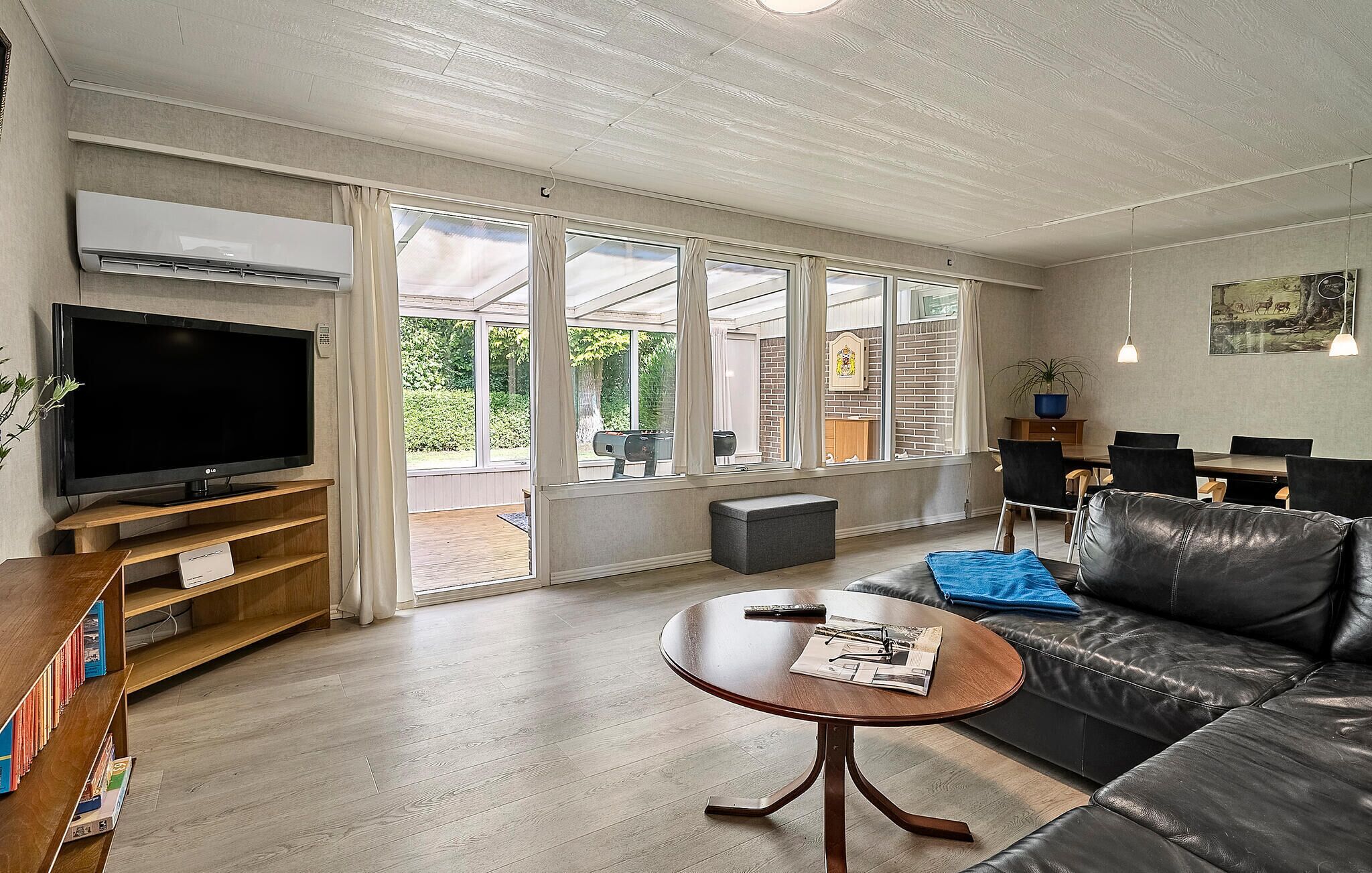A living room with a flat-screen TV, a leather sofa, a coffee table, and a dining area with a table and chairs.