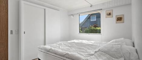 Une chambre à coucher avec un lit, une fenêtre donnant sur une maison et un luminaire au plafond.