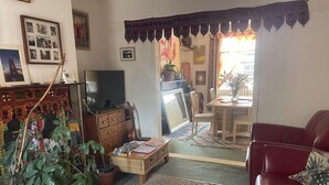Uma sala de estar com um sofá vermelho, uma televisão, um armário de madeira e um espaço de jantar com mesa e cadeiras.
