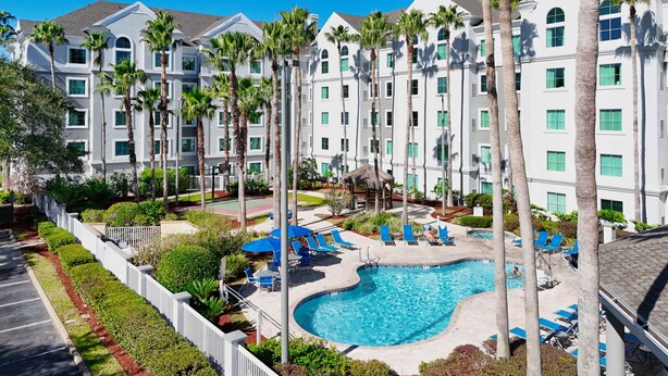 A resort with a swimming pool surrounded by palm trees and blue lounge chairs. - Disney Favorite FREE Shuttle (Orlando)