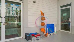 Entrada con puerta de vidrio y portón de metal, aro de baloncesto y un contenedor azul con balones de baloncesto naranja.