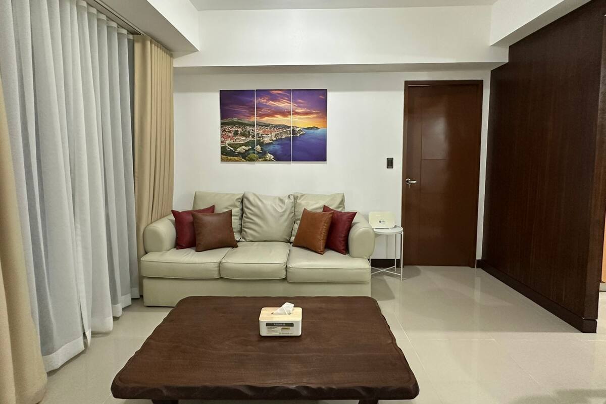 A modern living room with a beige sofa, a brown coffee table, and a cityscape painting on the wall.