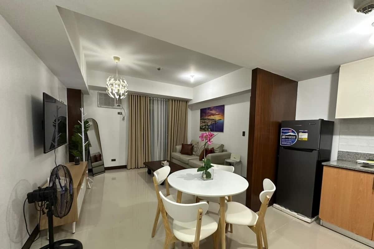 A modern living room with a dining area, a kitchen, and a TV mounted on the wall.