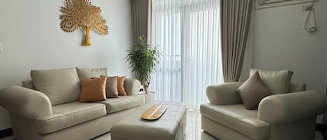 A modern living room with a beige sofa set, a coffee table, and a decorative tree wall art piece.