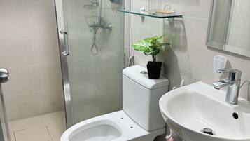 A modern bathroom with a glass-enclosed shower, a bidet, a toilet, a sink, and a potted plant.