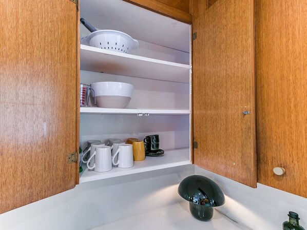 Een keuken met houten kastjes, een spoelbak en divers keukengerei, waaronder mokken en een vergiet.