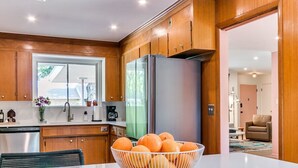 A modern kitchen with wooden cabinets, a stainless steel refrigerator, and a bowl of oranges on the counter. - Desert Rose: 1950s southwest modern home (Tulsa)