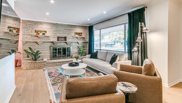 A modern living room with a stone fireplace, a sofa, a coffee table, and a large window with curtains. - Desert Rose: 1950s southwest modern home (Tulsa)