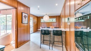 A modern kitchen with wooden cabinets, a central island with bar stools, and a large window providing natural light. - Desert Rose: 1950s southwest modern home (Tulsa)