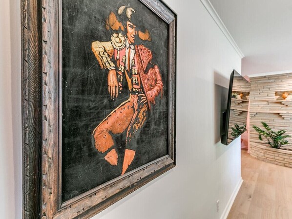 A framed artwork on a wall in a room with a wooden floor and a built-in TV shelf.