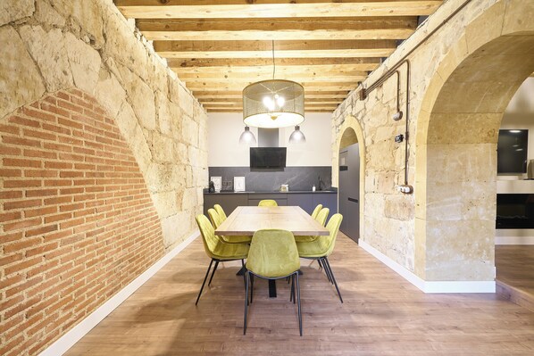 Un comedor con mesa de madera, sillas amarillas, paredes de ladrillo y vigas de madera a la vista.