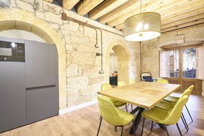 A modern kitchen with a large wooden table, yellow chairs, and stone walls.