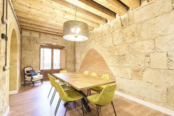 Un comedor con mesa de madera, sillas amarillas, una lámpara colgante y paredes de piedra.