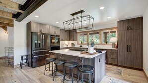 A modern kitchen with a central island, bar stools, stainless steel appliances, and a large window providing natural light.