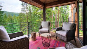A covered outdoor seating area with wicker chairs and a round table, overlooking a forested landscape.