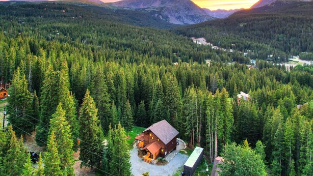 A cabin surrounded by dense forest with a mountain range in the background.