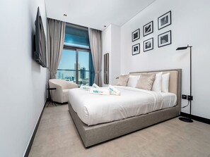 Una habitación de hotel moderna con una cama grande, un sofá, un televisor en la pared y vista a la ciudad.