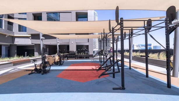 Academia ao ar livre com equipamentos de exercício, um tapete vermelho e um toldo.
