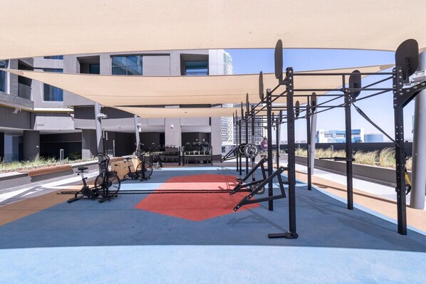 An outdoor gym with exercise equipment, a red mat, and a canopy.