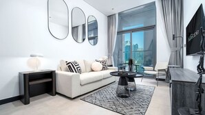 Uma sala de estar moderna com um sofá branco, almofadas preta e branca, uma mesa de centro de vidro e uma grande janela com vista para a cidade.