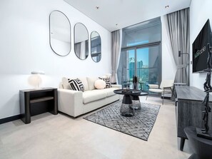 A modern living room with a white sofa, black and white cushions, a glass coffee table, and a large window offering a city view.