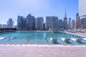 A swimming pool with lounge chairs and a city skyline in the background.