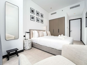 A modern bedroom with a large bed, a bedside table, a marble nightstand, a large wardrobe, and a mirror on the wall.