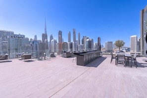 A rooftop terrace with modern furniture, a bar area, and a view of the Dubai skyline including the Burj Khalifa.