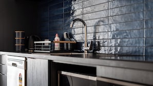 A modern kitchen with a stainless steel dishwasher, a built-in oven, and a black tiled backsplash. - City Centre Apartment on Hanover - Studio 1 (Dunedin)