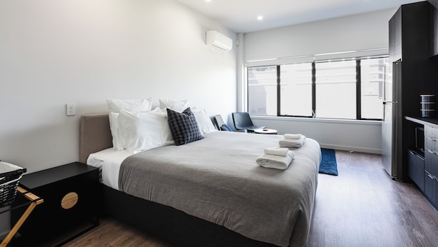 A modern hotel room with a large bed, a desk, a chair, and a TV. - City Centre Apartment on Hanover - Studio 1 (Dunedin)
