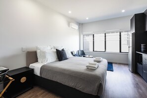 A modern hotel room with a large bed, a desk, a chair, and a TV. - City Centre Apartment on Hanover - Studio 1 (Dunedin)
