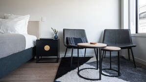 A modern hotel room with a bed, a small table with two chairs, a nightstand, and a view of the city through a window. - City Centre Apartment on Hanover - Studio 1 (Dunedin)