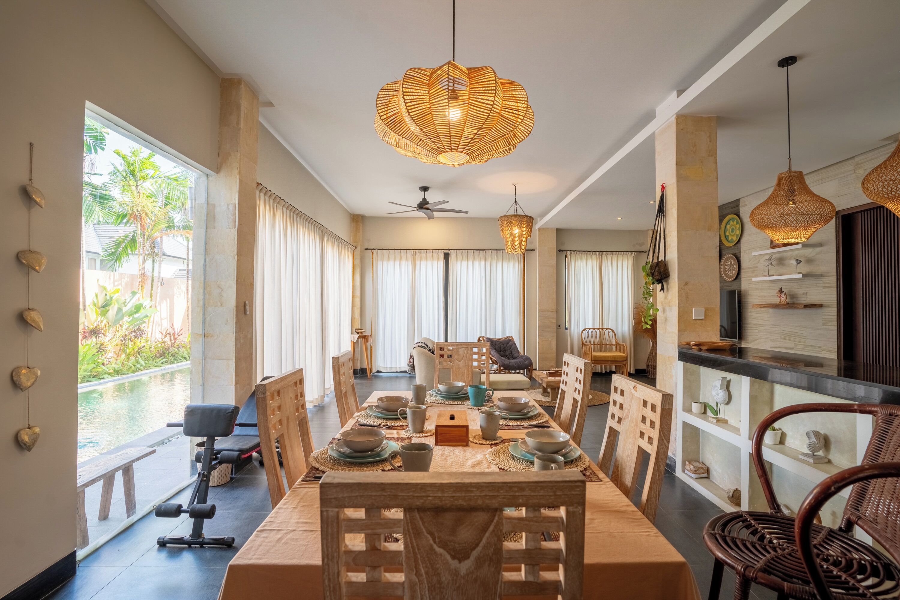 A dining area with a long table set for a meal, surrounded by chairs, with a ceiling fan and pendant lights above.